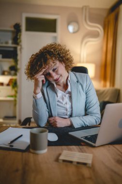 Kafkasyalı yetişkin bir kadın iş yerindeki masa başına oturmuş dizüstü bilgisayarla ilgili endişeleri okuyor e-posta okuyor ya da uzaktan kumandalı görevler yapan sorunlarla ilgili raporlar yazıyor.