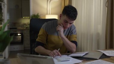 Genç, beyaz, genç bir erkek, gece veya akşam evde ders çalışıyor. Öğrenmeye karar veriyor. Dersi ya da sınavı tek başına yapıyor.