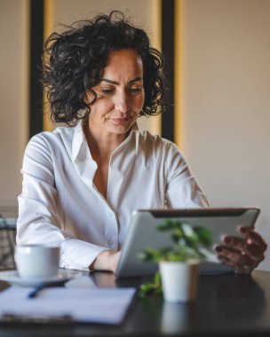 Bir kadın işkadını kafeteryada ya da restoran yöneticisinin masasında oturuyor. İş yerinde dijital tablet kullanıyor. İş yapan yetişkin bir kadın girişimci.
