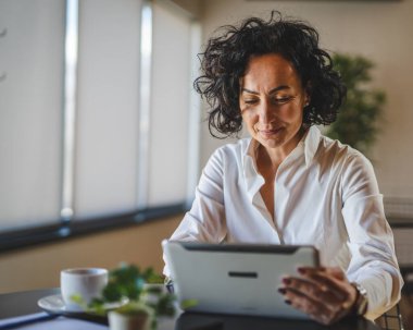 Bir kadın işkadını kafeteryada ya da restoran yöneticisinin masasında oturuyor. İş yerinde dijital tablet kullanıyor. İş yapan yetişkin bir kadın girişimci.