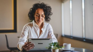 Bir kadın işkadını kafeteryada ya da restoran yöneticisinin masasında oturuyor. İş yerinde dijital tablet kullanıyor. İş yapan yetişkin bir kadın girişimci.