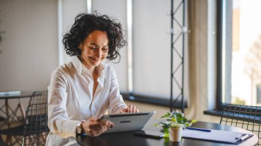Bir kadın işkadını kafeteryada ya da restoran yöneticisinin masasında oturuyor. İş yerinde dijital tablet kullanıyor. İş yapan yetişkin bir kadın girişimci.