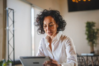 Bir kadın işkadını kafeteryada ya da restoran yöneticisinin masasında oturuyor. İş yerinde dijital tablet kullanıyor. İş yapan yetişkin bir kadın girişimci.