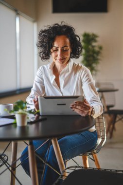 Bir kadın işkadını kafeteryada ya da restoran yöneticisinin masasında oturuyor. İş yerinde dijital tablet kullanıyor. İş yapan yetişkin bir kadın girişimci.