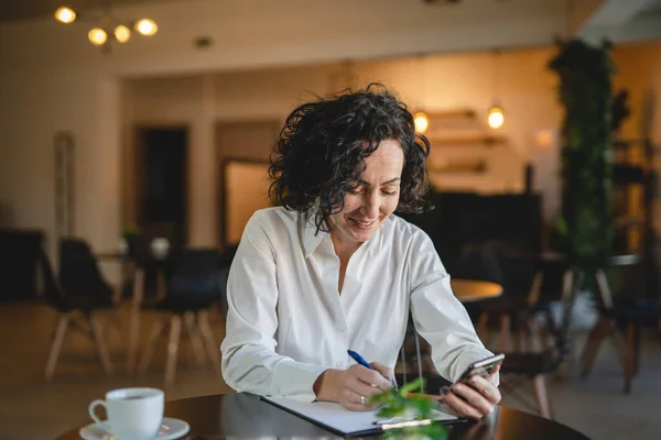 1人の女性ビジネス女性はカフェやレストランのマネージャーでテーブルに座る仕事でスマートフォンの携帯電話を使用成熟した女性起業家ビジネスをオンラインで行う実際の人がスペースをコピー書き込み — ストック写真