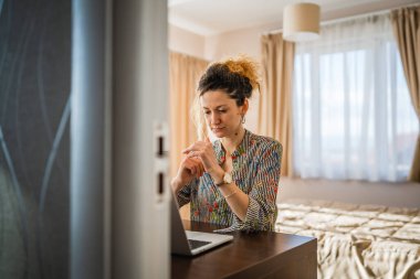 Yetişkin bir kadın beyaz kadın yatak odasında ya da otel odasında dizüstü bilgisayarda çalışıyor.