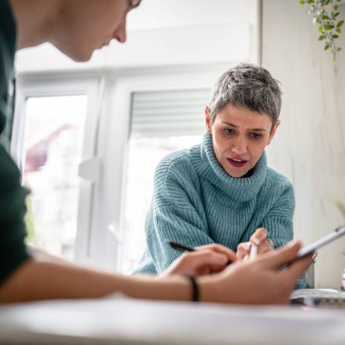 One student teenage caucasian man study learn with help of his tutor professor or mother senior woman at home having private lesson to prepare for exam education concept real people copy space