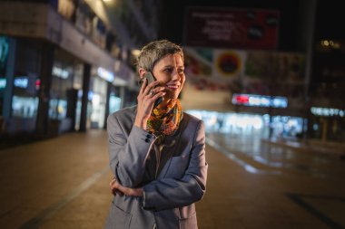 Kıdemli bir kadın, kısa beyaz saçlı, beyaz bir kadın konuşmak için cep telefonu kullanıyor ya da şehirde bir telefon görüşmesi yapıyor. Mutlu bir gülümseme, kendine güvenen gerçek bir insanı taklit ediyor.