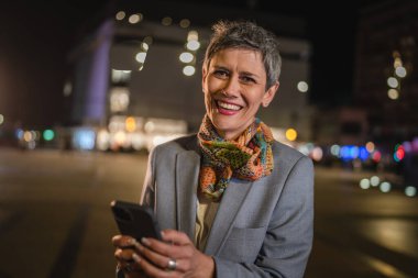 Kıdemli bir kadın, kısa gri saçlı, beyaz bir kadın, cep telefonunu internet üzerinden video görüşmesi yapmak ya da mesajlar göndermek için kullanır. Mutlu bir gülümseme, kendine güvenen gerçek bir insanı taklit etmek için.