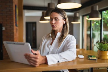 Yetişkin yetişkin bir kadın Kafkas kadın girişimci yönetici evde ya da iş yerinde masa başında dururken dijital tablet kullanıyor ve beyaz gömlek fotokopi alanı giyiyor