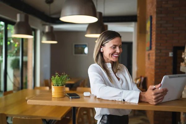 一位成年女性工作时使用数码平板电脑 站在家中或工作场所的餐桌旁 穿着白衬衫复制空间快乐地笑着 — 图库照片