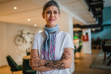 Kafeteryada ya da restoranda tek başına duran, beyaz gömlekli, kendine güvenen, mutlu, mutlu gülümseyen, kısa gri saçlı, modern görünümlü bir kadın.