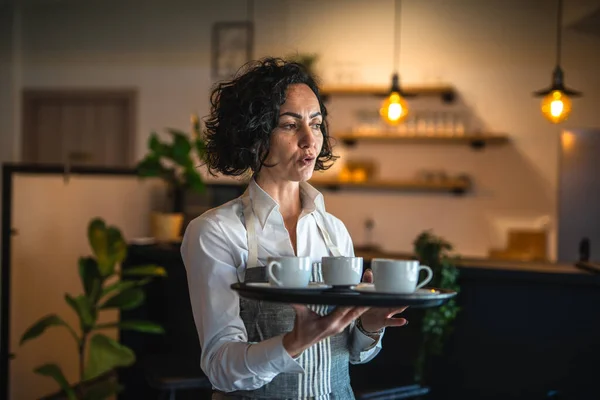 One mature woman caucasian waitress at cafe or restaurant carry tray with coffee female entrepreneur at work real people copy space small business concept