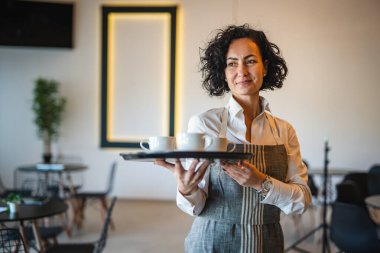 Kafe ya da lokantada çalışan olgun bir kadın garson kahve tepsisi taşıyor. İş yerindeki bayan girişimci. Gerçek insanlar uzay küçük işletme konseptini kopyalıyor.