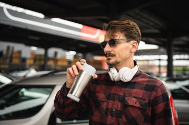 Yetişkin bir beyaz erkek, işe giderken arabanın yanında duruyor. Gerçek insanlar iş yerine giderken ya da giderken bir fincan kahve tutuyor.