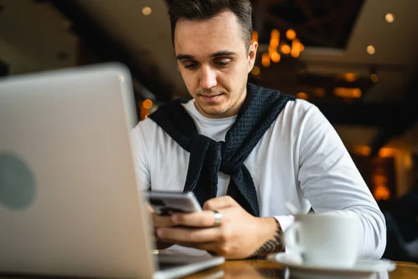 カフェやレストランのテーブルに座っている1人の男は インターネットの閲覧やテキストメッセージのための携帯電話を使用してカジュアルを身に着けています — ストック写真