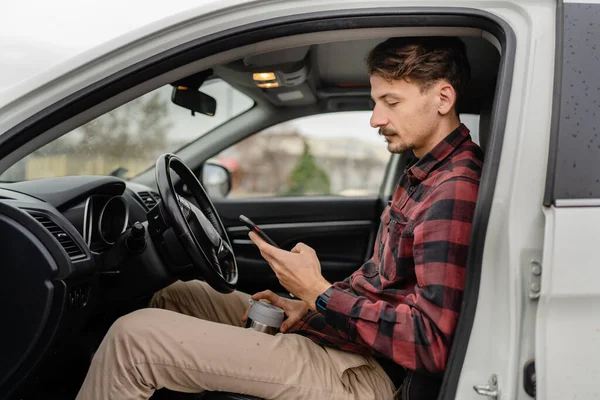 車の中で座って口ひげを生やしている1人の男白人男性は 道路上でブレーキを取ります旅行のホールドカップコーヒーは Smsテキストメッセージやナビゲーションアプリのための携帯電話のスマートフォンを使用して 実際の人々はスペースをコピー — ストック写真