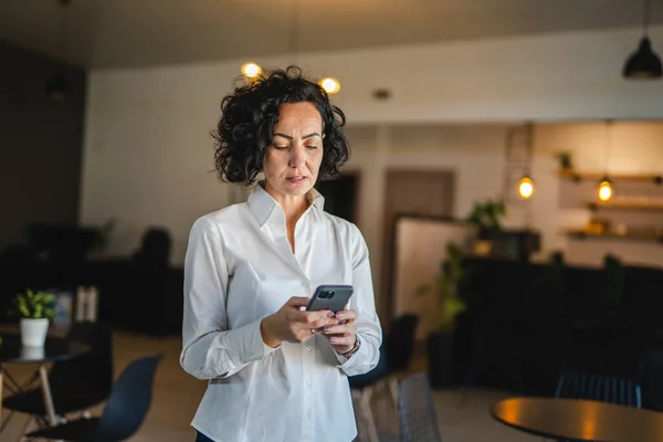 一人の成熟した女性は自宅や職場でスマートフォンを使用します欲求不満狂 — ストック写真