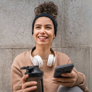 Kulaklık takan bir genç kadın destek şişesi ve akıllı telefon, spor, Kafkasyalı bir kadın Z jenerasyonu sağlıklı yaşam tarzı konseptini kopyalamak için fren yapıyor.