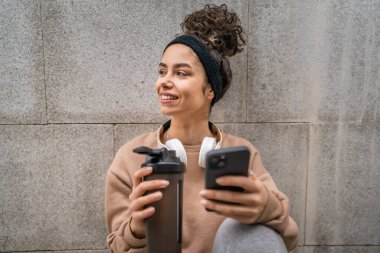 Kulaklık takan bir genç kadın destek şişesi ve akıllı telefon, spor, Kafkasyalı bir kadın Z jenerasyonu sağlıklı yaşam tarzı konseptini kopyalamak için fren yapıyor.