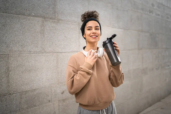 stock image One young woman with headphones prepare for training hold supplement shaker bottle to drink water stand outdoor beautiful sporty caucasian female generation z healthy lifestyle concept copy space