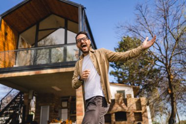 Kafkasyalı yetişkin bir erkek modern küçük ev sahibinin ya da pazarlamacının önünde duruyor. El hareketleriyle davetkar bir gülümsemeye davet ediliyor. Güneşli bir günde mutlu bir gülümseme.