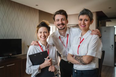 İş konferansına hazırlanan bir grup insanın ön manzara portresi. Erkekler ve kadınlar otel odasında kameraya gülümseyen, gülümseyen, gülümseyen, beyaz tişörtler giyen insanlar.