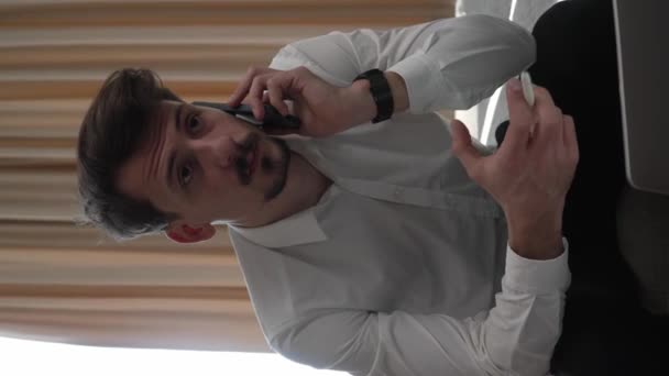 ホテルの部屋からラップトップコンピュータ上で1人の男の大人の白人男性の仕事は ビジネス旅行のコピースペースで口ひげと白いシャツを身に着けていますリモートビジネスマンの概念は 電話で話をする — ストック動画