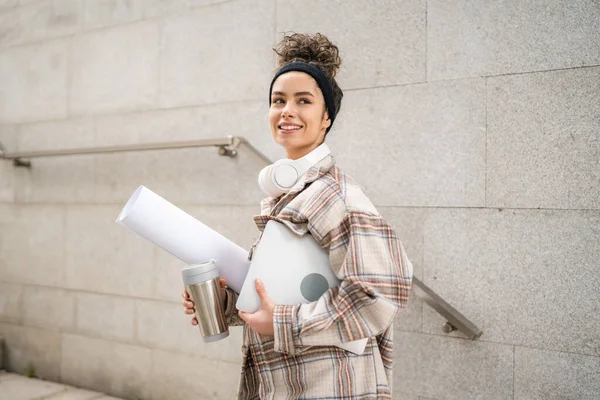 stock image One woman young adult female student go to class outdoor hold laptop computer cup of coffee and work material real person coy space happy smile confident with headphones in day