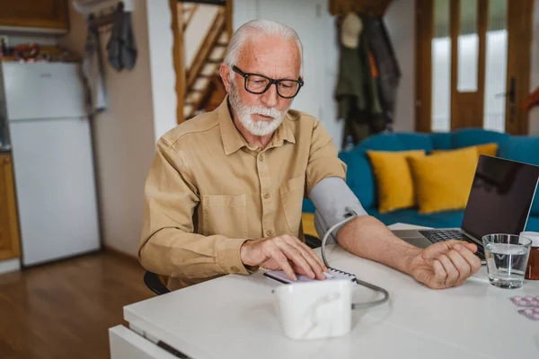 One man senior caucasian male with beard use blood pressure device to check and measure results while sit at the table at home alone real people copy space health care concept