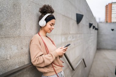 Genç bir yetişkin nesil z beyaz kulaklıklı ve ip atlayan modern kadın mutlu bir gülümseme eğitim için cep telefonu uygulaması kullanın ya da şehirde müzik bakımı yapın gerçek bir insan uzayı kopyalasın