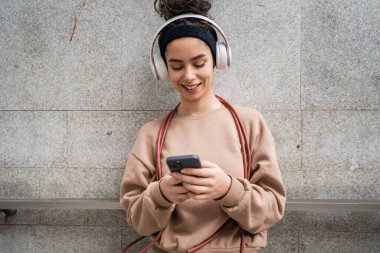 Genç bir yetişkin nesil z beyaz kulaklıklı ve ip atlayan modern kadın mutlu bir gülümseme eğitim için cep telefonu uygulaması kullanın ya da şehirde müzik bakımı yapın gerçek bir insan uzayı kopyalasın