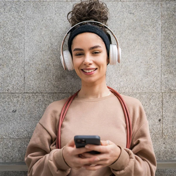 Genç bir yetişkin nesil z beyaz kulaklıklı ve ip atlayan modern kadın mutlu bir gülümseme eğitim için cep telefonu uygulaması kullanın ya da şehirde müzik bakımı yapın gerçek bir insan uzayı kopyalasın