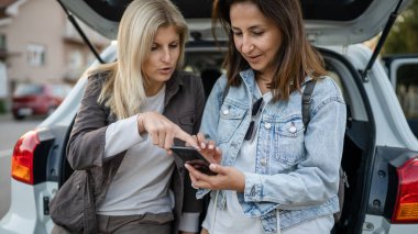 İki olgun kadın Kafkasyalı kız arkadaş mobil telefon tatil konseptini kontrol ediyor online harita planlama araba otomobili o gün gerçek insanlar uzay akıllı telefon uygulaması ve GPS kopyalamak