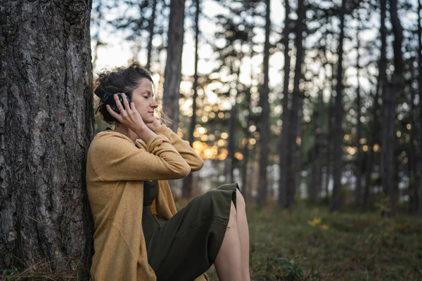一人で公園や森の中に座っている一人の女性の若い大人の白人女性とヘッドフォンガイド付き瞑想セルフケア症状の練習精神的な感情的なバランスの概念を準備 — ストック写真