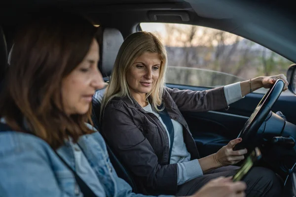 車の中で2人の女性成熟した女性の白人の友人は 携帯電話の休暇の概念をチェックしますオンライン地図は 実際の人々は スペースのスマートフォンアプリとGpsをコピーし 自動車での旅行ルートを計画 — ストック写真