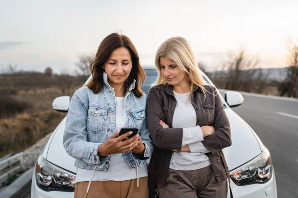 2人の女性成熟した女性の白人の友人は 携帯電話の休暇の概念をチェックオンライン地図の計画車での旅行ルート実際の人々は スペースのスマートフォンアプリとGpsをコピーします — ストック写真