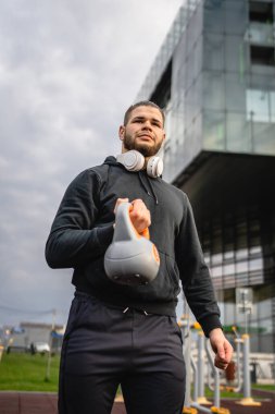 Kafkasyalı genç bir erkek sporcu gün içinde dışarıda Rus çanı Girya Kettlebell ağırlığında gerçek bir insan gibi poz veriyor.