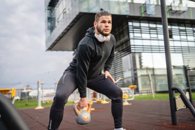 Kafkasyalı genç bir erkek sporcu gün içinde dışarıda Rus çanı Girya Kettlebell ağırlık egzersizi ile antrenman yapıyor.