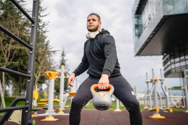 Kafkasyalı genç bir erkek sporcu gün içinde dışarıda Rus çanı Girya Kettlebell ağırlık egzersizi ile antrenman yapıyor.
