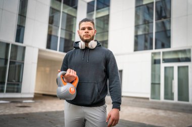 Kafkasyalı genç bir erkek sporcu gün içinde dışarıda Rus çanı Girya Kettlebell ağırlığında gerçek bir insan gibi poz veriyor.