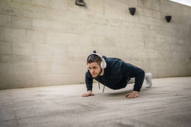 Genç bir yetişkin beyaz erkek dışarıda şınav çekiyor.