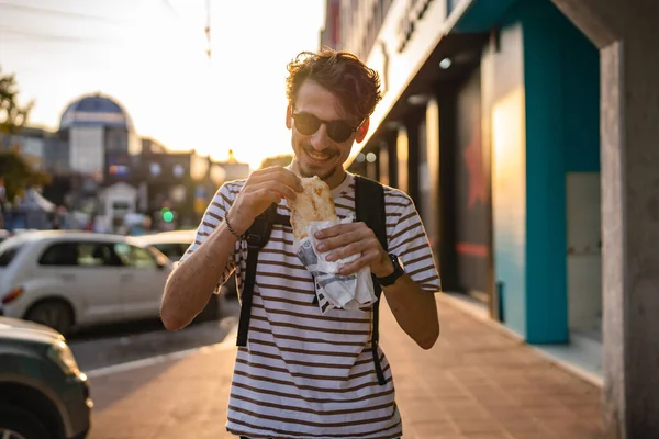 晴れた日の散歩で街の一人の若い大人の現代的な白人男性とサンドイッチを食べるファーストフードのコンセプト都市生活コピースペース観光客が路上で食べる実際の人 — ストック写真