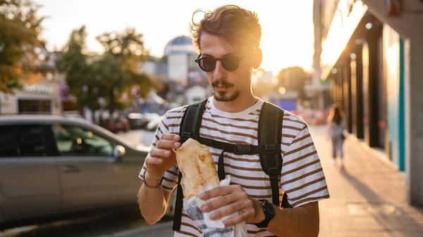 晴れた日の散歩で街の一人の若い大人の現代的な白人男性とサンドイッチを食べるファーストフードのコンセプト都市生活コピースペース観光客が路上で食べる実際の人 — ストック写真