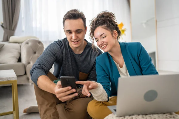 男人和女人坐在家里的地板上 一边阅读短信 一边上网浏览手机 一边在网上聊天 — 图库照片