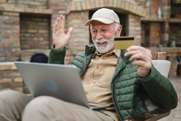 stock image One man senior caucasian male with beard sit outdoor in day with laptop computer making online purchase shopping buy stuff hold credit card pensioner enjoy his retirement copy space real person