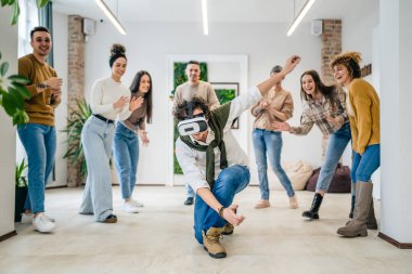 Yetişkin bir beyaz erkek, bir grup erkek ve kadın arkadaşın önünde sanal gerçeklik cihazının keyfini çıkarıyor. Takım oluşturma semineri sırasında birlikte eğleniyorlar. Gerçek insanlar parlak filtreler.