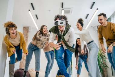 Yetişkin bir beyaz erkek, bir grup erkek ve kadın arkadaşın önünde sanal gerçeklik cihazının keyfini çıkarıyor. Takım oluşturma semineri sırasında birlikte eğleniyorlar. Gerçek insanlar parlak filtreler.