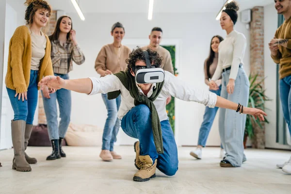 Yetişkin bir beyaz erkek, bir grup erkek ve kadın arkadaşın önünde sanal gerçeklik cihazının keyfini çıkarıyor. Takım oluşturma semineri sırasında birlikte eğleniyorlar. Gerçek insanlar parlak filtreler.