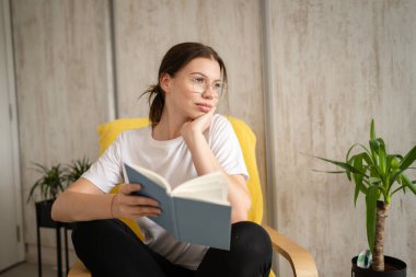 Genç bir kadın, beyaz kadın, evinde oturmuş kitap okuyor. Mekan fotokopisi çekiyor. Gerçek insanlar hafta sonları boş vakit geçiriyorlar.